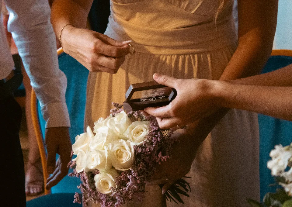 Braut mit einem Strauß weißer Rosen, die einen Ehering aus einem kleinen Ringkästchen nimmt.