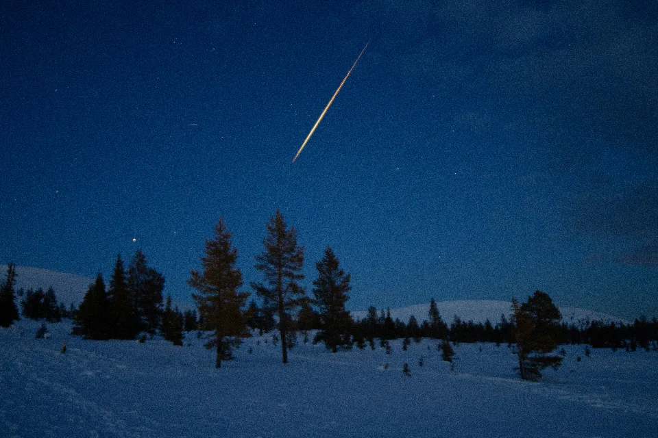 Heller Meteorstreifen am Nachthimmel über verschneiten Bäumen und einer Winterlandschaft im Pallas-Yllästunturi-Nationalpark, Finnland.